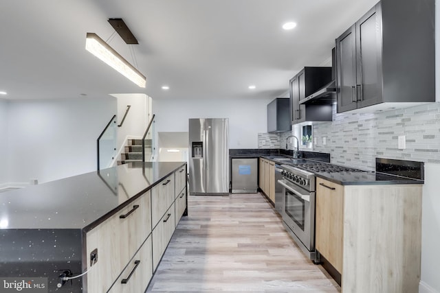 kitchen featuring appliances with stainless steel finishes, dark stone counters, light hardwood / wood-style floors, and sink