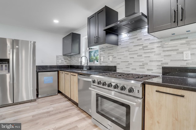 kitchen featuring appliances with stainless steel finishes, light wood-type flooring, light brown cabinetry, and wall chimney range hood