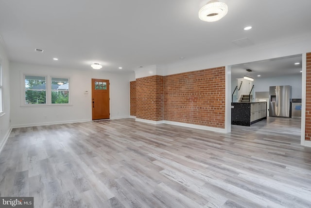 unfurnished living room with brick wall and light hardwood / wood-style flooring