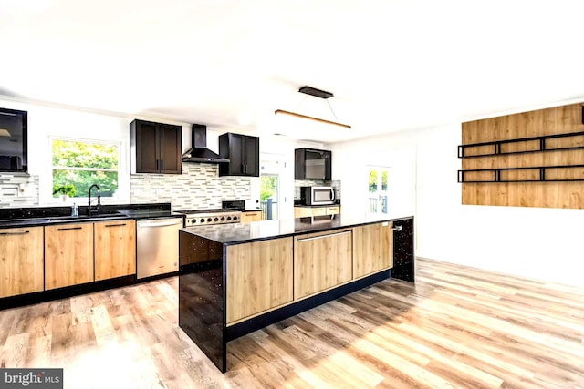 kitchen featuring light hardwood / wood-style floors, a kitchen island, wall chimney exhaust hood, stainless steel appliances, and decorative backsplash