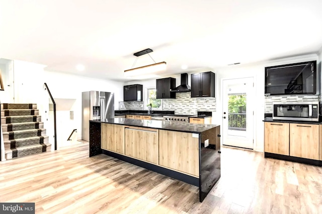 kitchen featuring appliances with stainless steel finishes, light brown cabinetry, wall chimney range hood, and plenty of natural light