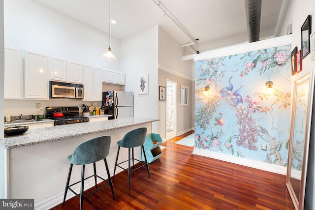 kitchen featuring dark hardwood / wood-style flooring, appliances with stainless steel finishes, a kitchen bar, white cabinetry, and light stone counters