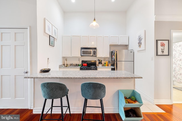 kitchen featuring pendant lighting, white cabinetry, appliances with stainless steel finishes, hardwood / wood-style flooring, and a breakfast bar area