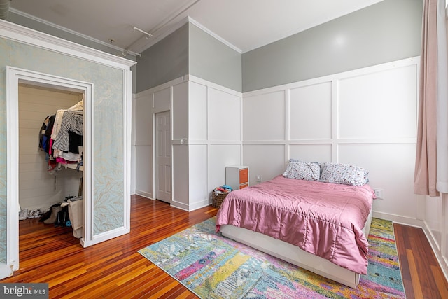 bedroom with dark wood-type flooring, ornamental molding, a spacious closet, and a closet