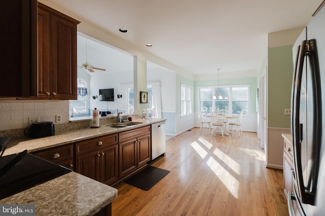 kitchen with ceiling fan with notable chandelier, stainless steel appliances, sink, pendant lighting, and light hardwood / wood-style flooring