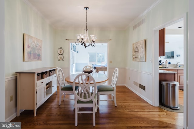 dining area with hardwood / wood-style flooring, ornamental molding, and a notable chandelier