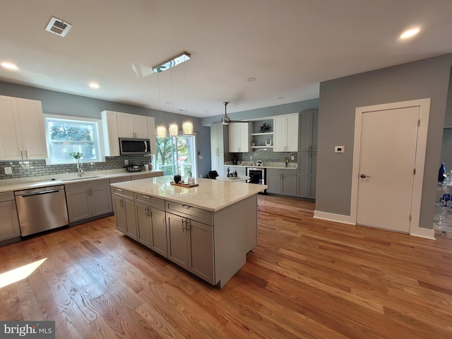 kitchen featuring a kitchen island, appliances with stainless steel finishes, hanging light fixtures, and gray cabinetry