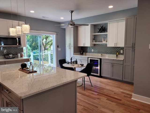 kitchen with wine cooler, decorative light fixtures, gray cabinets, light hardwood / wood-style floors, and decorative backsplash