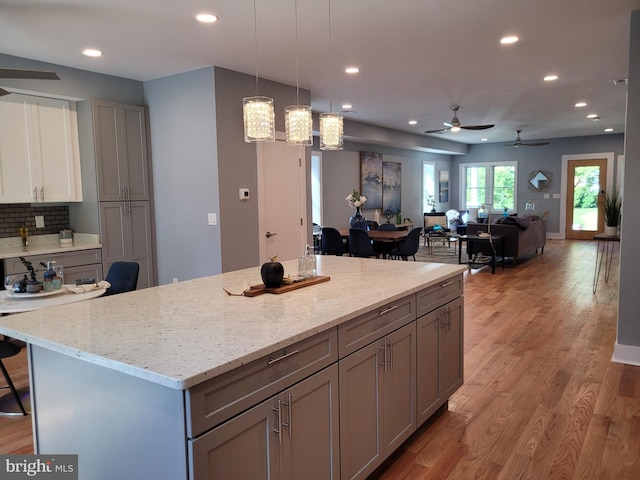 kitchen with gray cabinetry, tasteful backsplash, pendant lighting, ceiling fan, and light hardwood / wood-style flooring