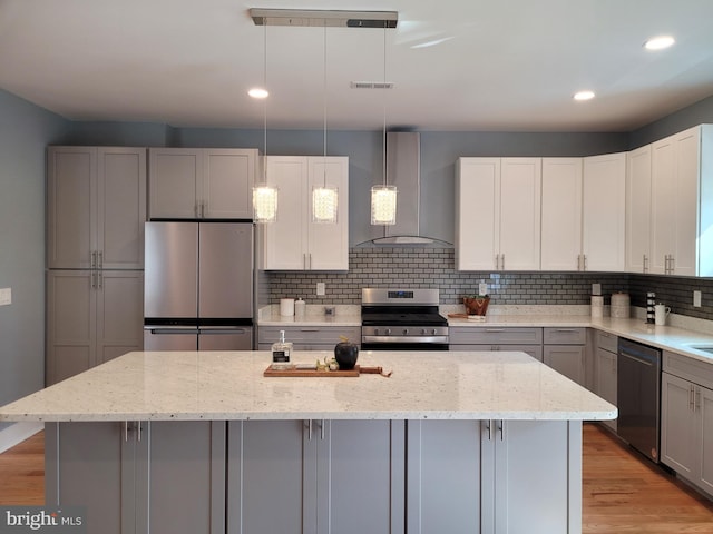 kitchen featuring wall chimney exhaust hood, stainless steel appliances, a center island, and pendant lighting