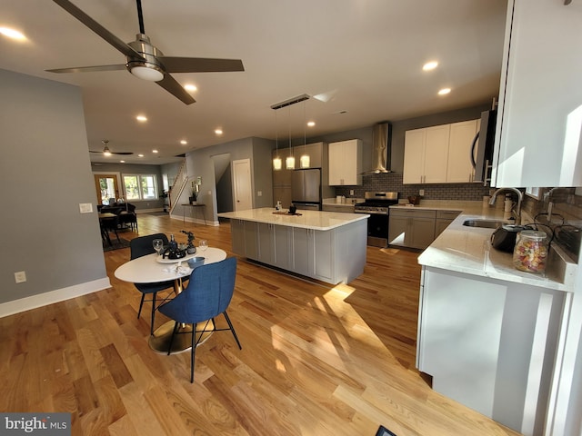 kitchen with appliances with stainless steel finishes, wall chimney exhaust hood, a kitchen island, ceiling fan, and decorative light fixtures