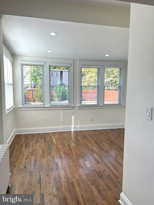 empty room featuring dark hardwood / wood-style flooring, a wealth of natural light, and radiator heating unit