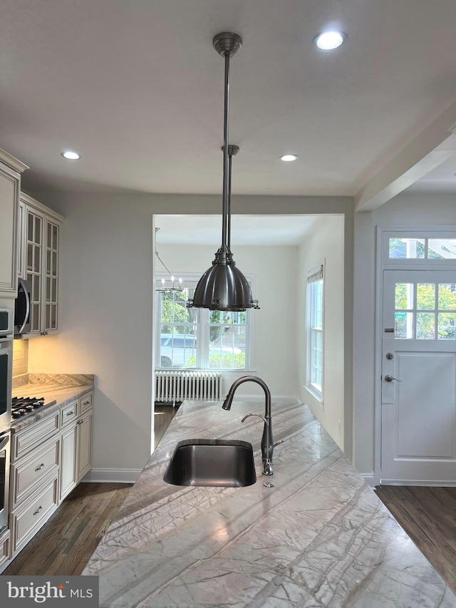 kitchen featuring radiator heating unit, stainless steel appliances, decorative light fixtures, hardwood / wood-style floors, and sink