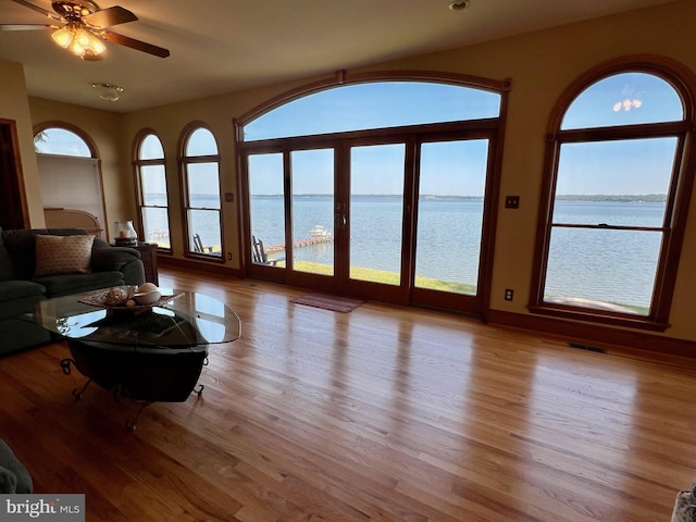 unfurnished living room featuring ceiling fan, light hardwood / wood-style floors, and a water view