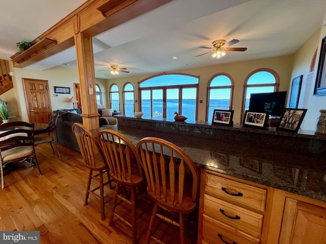 kitchen with a water view, dark stone countertops, ceiling fan, and light hardwood / wood-style flooring