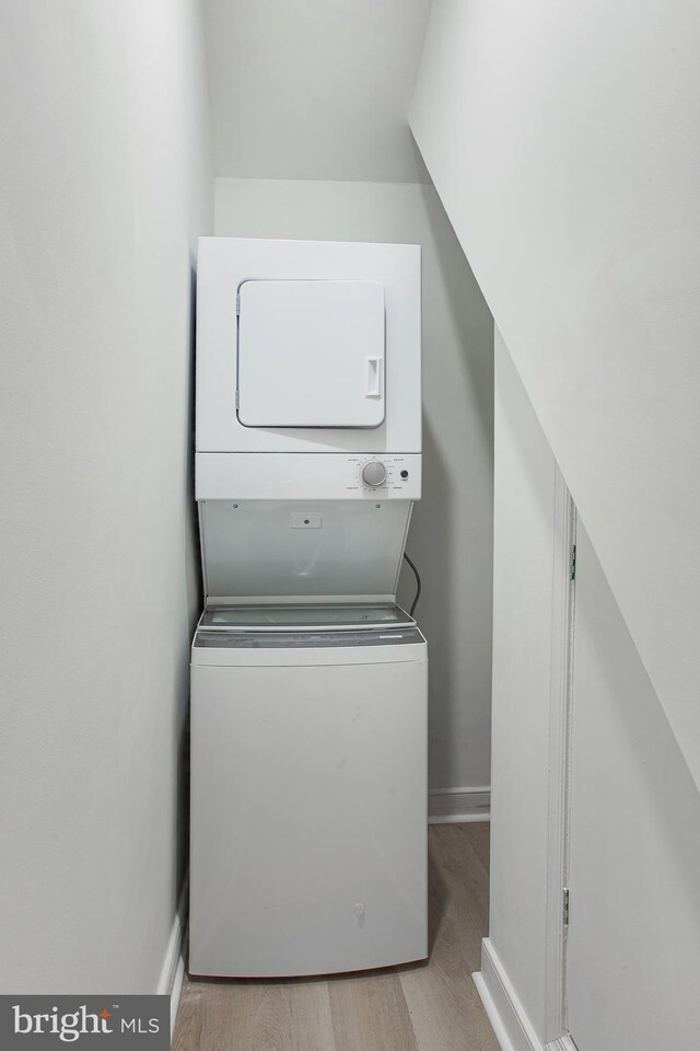 laundry area with stacked washer / drying machine and light hardwood / wood-style floors