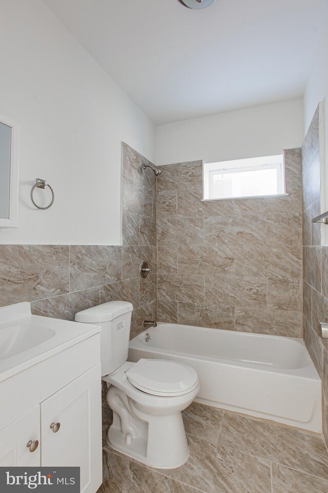 full bathroom featuring tile walls, toilet, tiled shower / bath combo, and vanity