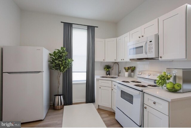 kitchen with white appliances, backsplash, sink, white cabinetry, and light wood-type flooring