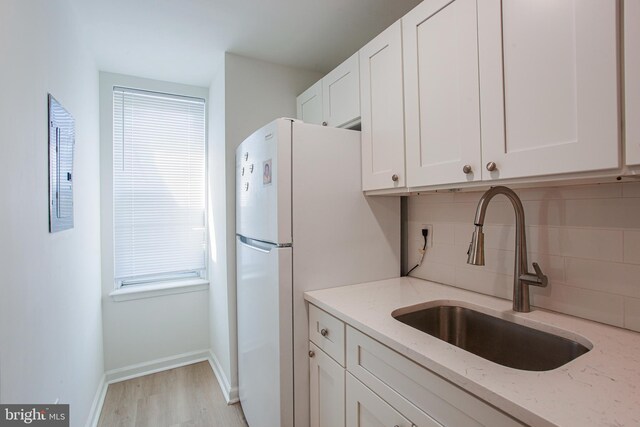 kitchen featuring white cabinetry, backsplash, sink, light stone countertops, and light hardwood / wood-style floors