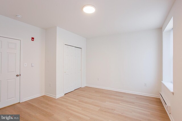 unfurnished bedroom with a closet, a baseboard radiator, and light hardwood / wood-style floors