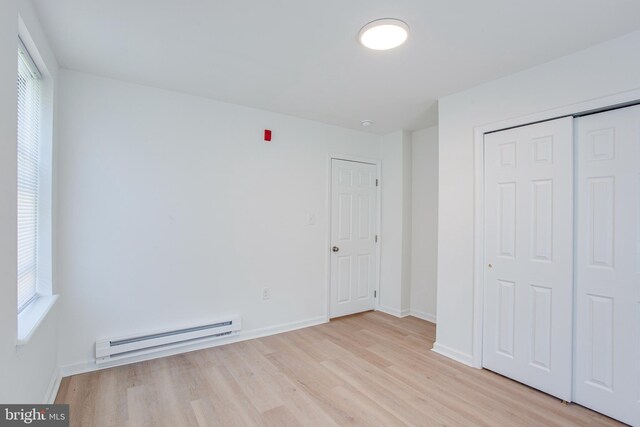 unfurnished bedroom with light wood-type flooring, a closet, and baseboard heating