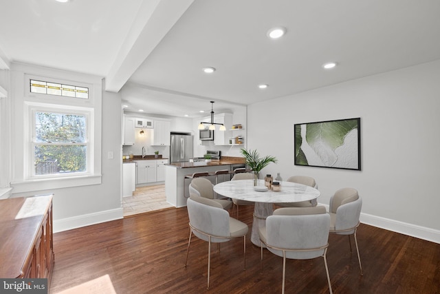 dining room with beam ceiling, sink, and dark hardwood / wood-style flooring