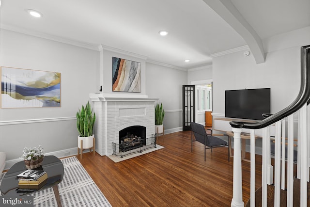 living room featuring beamed ceiling, wood-type flooring, ornamental molding, and a fireplace