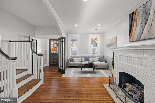 living room with dark wood-type flooring, a chandelier, crown molding, and a brick fireplace