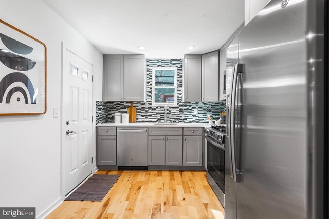 kitchen featuring light hardwood / wood-style floors, sink, gray cabinetry, stainless steel appliances, and decorative backsplash