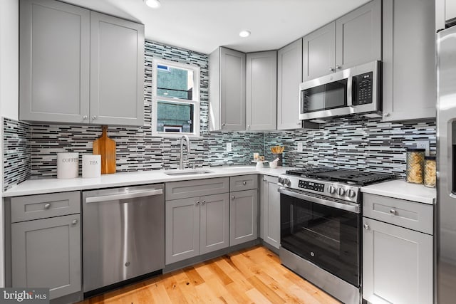 kitchen with appliances with stainless steel finishes, decorative backsplash, gray cabinets, light wood-type flooring, and sink