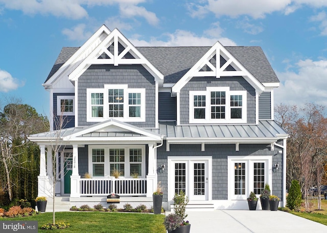 view of front of property featuring a shingled roof, a front lawn, covered porch, metal roof, and a standing seam roof