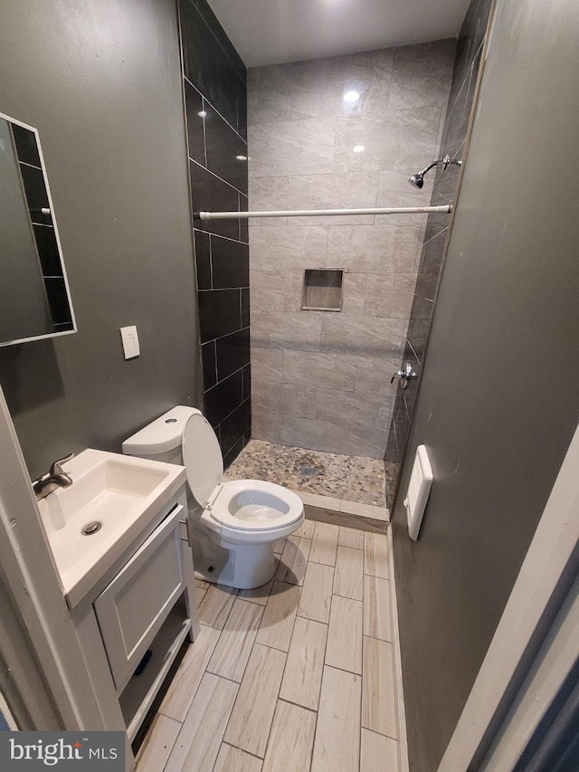 bathroom featuring tiled shower, toilet, and vanity