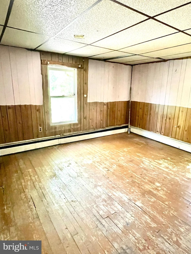 spare room featuring a baseboard heating unit, wood walls, wood-type flooring, and a drop ceiling