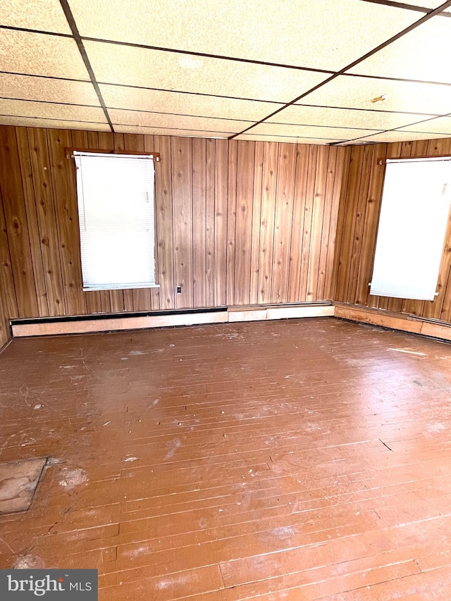 spare room featuring a drop ceiling, wood walls, and wood-type flooring