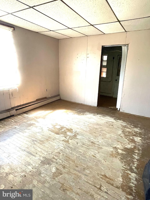 empty room featuring hardwood / wood-style floors, baseboard heating, and a drop ceiling