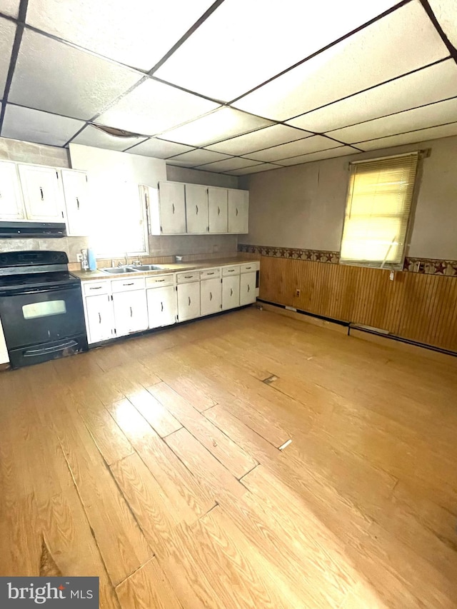 kitchen with light wood-style floors, wainscoting, black electric range oven, and white cabinetry