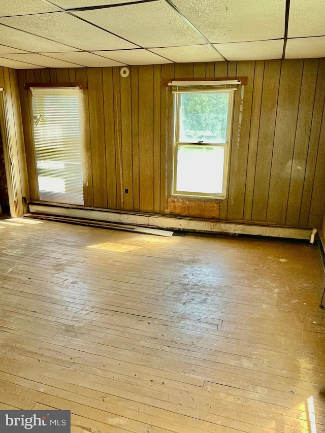 empty room with a paneled ceiling, light wood-type flooring, and wooden walls