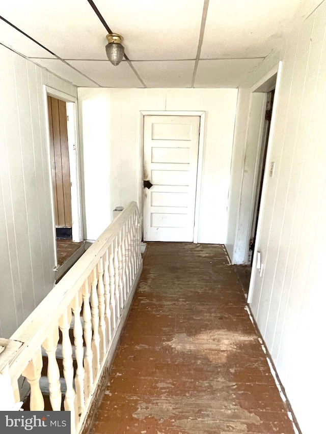 hallway featuring an upstairs landing, a paneled ceiling, and wood walls