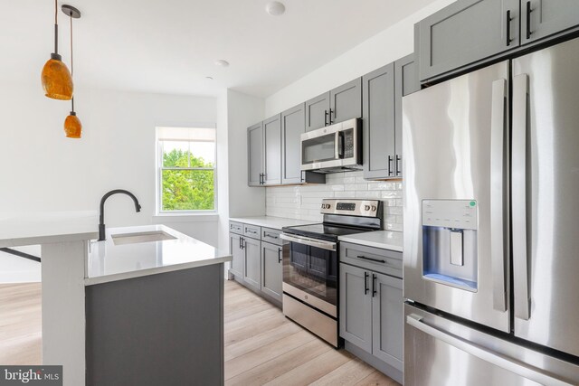 kitchen featuring gray cabinetry, decorative light fixtures, stainless steel appliances, sink, and light wood-type flooring