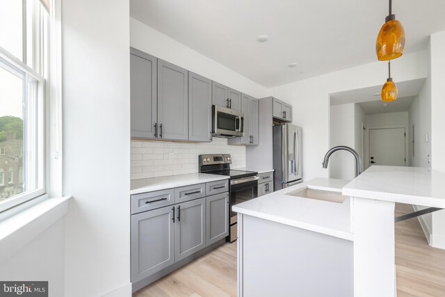 kitchen featuring pendant lighting, light stone counters, sink, appliances with stainless steel finishes, and light hardwood / wood-style floors