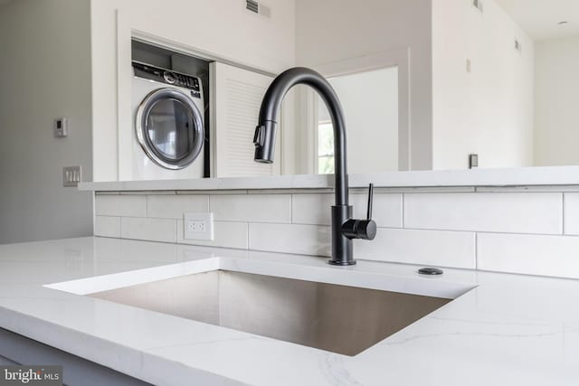 room details with washer / clothes dryer, light stone counters, sink, and tasteful backsplash