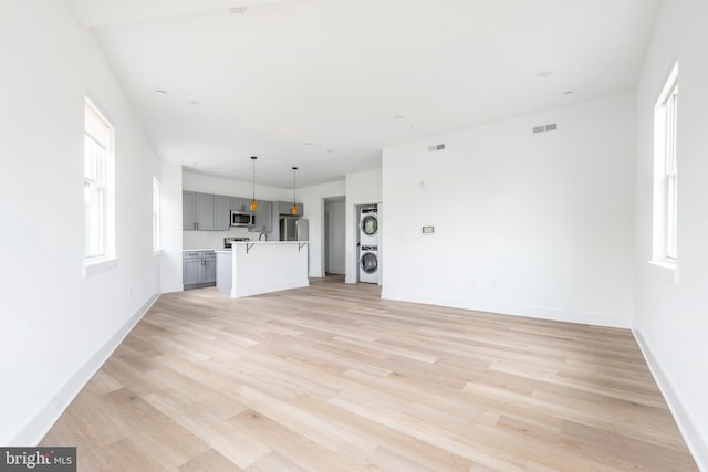 unfurnished living room with stacked washer / dryer and light wood-type flooring