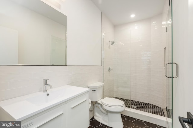 bathroom featuring toilet, a shower with door, tile patterned flooring, vanity, and tile walls