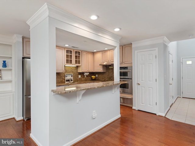 kitchen featuring sink, light stone counters, a breakfast bar area, appliances with stainless steel finishes, and hardwood / wood-style flooring