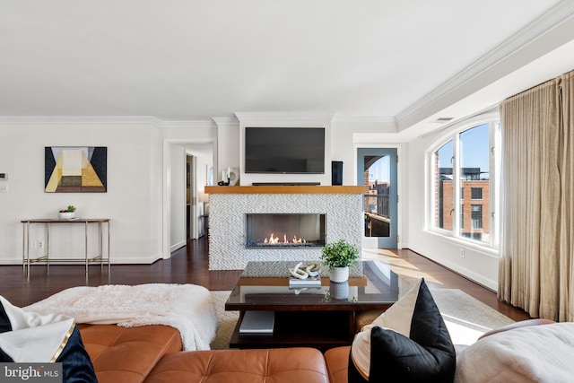 living area with baseboards, wood finished floors, a tiled fireplace, and crown molding