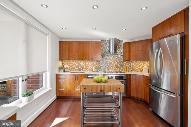 kitchen with brown cabinetry, stainless steel appliances, wall chimney exhaust hood, and a sink