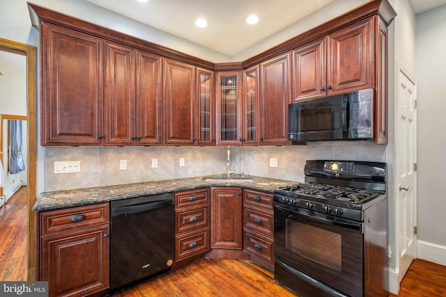 kitchen with hardwood / wood-style flooring, sink, black appliances, dark stone counters, and decorative backsplash