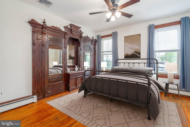 bedroom with a baseboard heating unit, ceiling fan, light wood-type flooring, and multiple windows