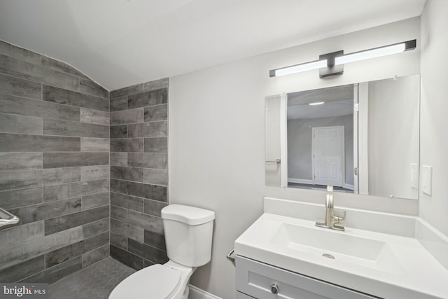 bathroom featuring a tile shower, vanity, lofted ceiling, and toilet