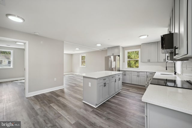 kitchen featuring gray cabinetry, a kitchen island, hardwood / wood-style flooring, stainless steel refrigerator with ice dispenser, and sink